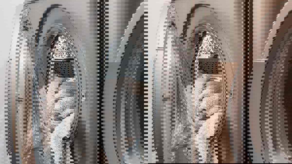 En sølvfarvet vaskemaskine. Der ligger et håndklæde i maskinen, som lågen ikke er lukket på endnu.